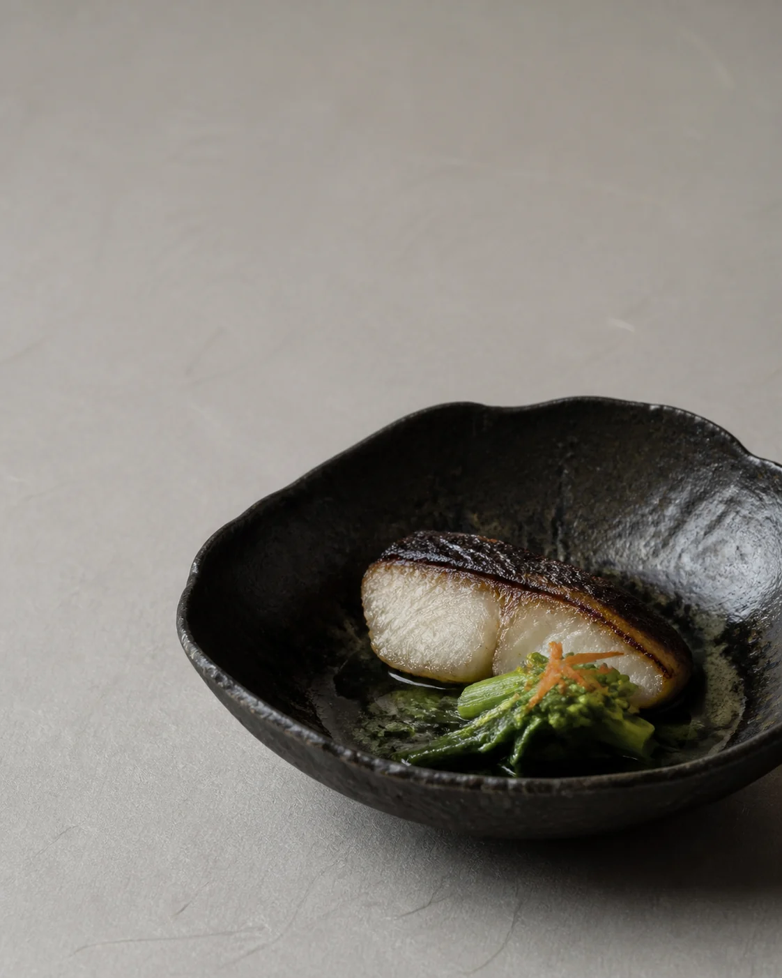 Charcoal-grilled black cod and spring greens in a handmade dark ceramic bowl