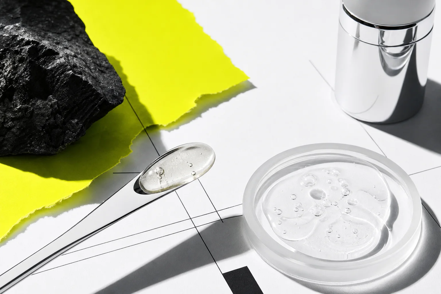Clear skincare gel, chrome spatula and black mineral sample on a laboratory grid